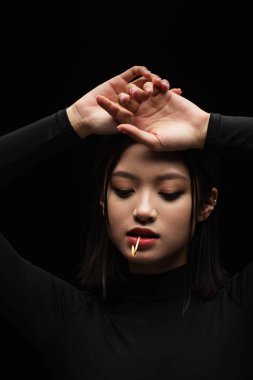 portrait of pretty asian model with burning match in mouth posing isolated on black clipart
