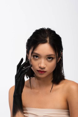 young asian woman with bare shoulders and hand in black paint posing isolated on white