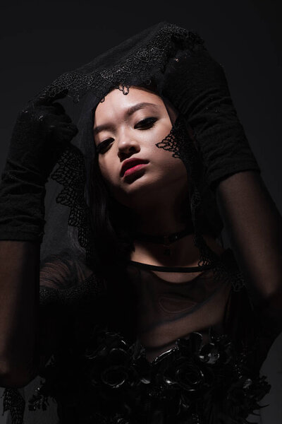portrait of asian model in black gloves holding black veil isolated on grey