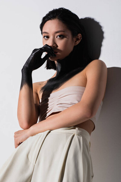 young asian woman with hand in black paint looking at camera on white