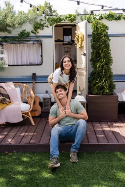 Positive woman hugging boyfriend near camper outdoors 