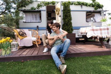 Smiling woman embracing boyfriend on terrace near camper outdoors 