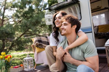 Smiling woman holding hands of boyfriend near camper outdoors 
