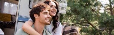 Cheerful woman hugging brunette boyfriend near camper van outdoors, banner 