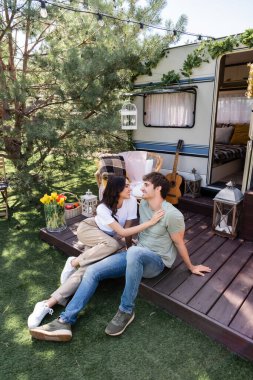 Side view of smiling woman touching boyfriend on terrace of camper van 