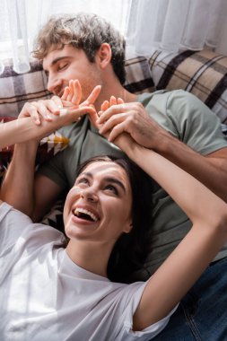 High angle view of smiling woman touching hands of blurred boyfriend on bed in camper van 