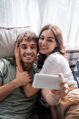 Brunette woman hugging boyfriend taking selfie on smartphone in camper van 