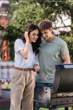 Positive couple with wine cooking on grill outdoors 