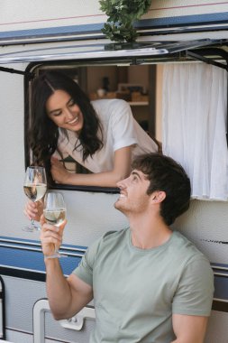 Smiling man holding glass of wine near girlfriend in camper van 
