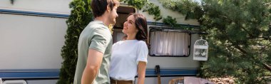Cheerful brunette woman looking at boyfriend on terrace near camper van, banner 
