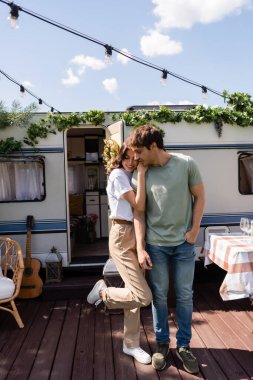 Smiling woman hugging boyfriend under light bulbs on terrace near camper van 