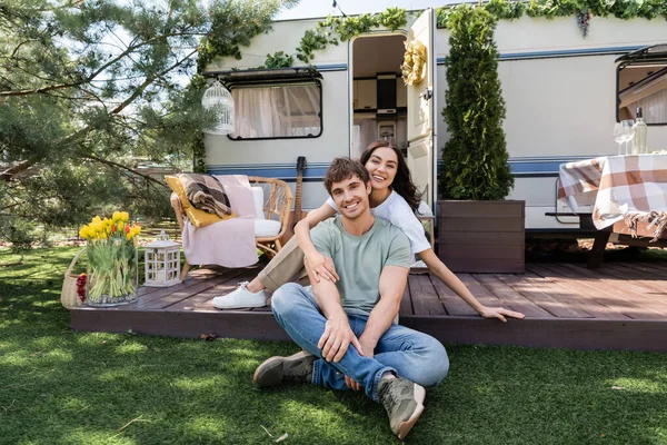 Smiling woman hugging boyfriend and looking at camera on terrace of camper van 