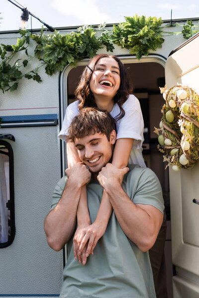 Cheerful woman hugging brunette boyfriend near decor on camper van 