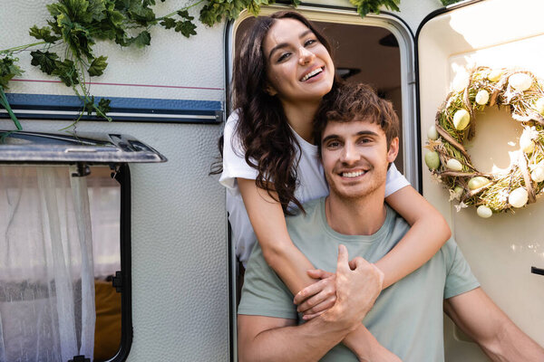 Positive woman embracing boyfriend near door of camper van outdoors 