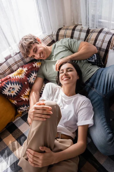 High angle view of cheerful man touching hair of girlfriend on bed in camper van