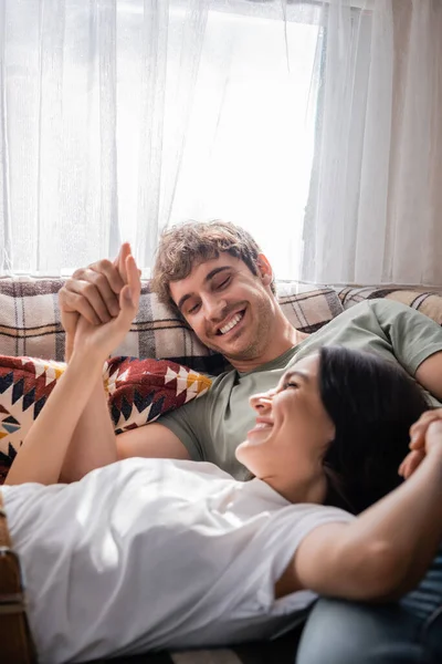 Positive couple holding hands while lying on bed in camper van
