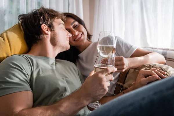 Positive couple holding wine and resting on bed in camper van