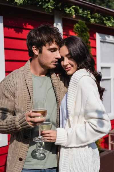 Man in knitted cardigan holding glass of wine near girlfriend and building outdoors