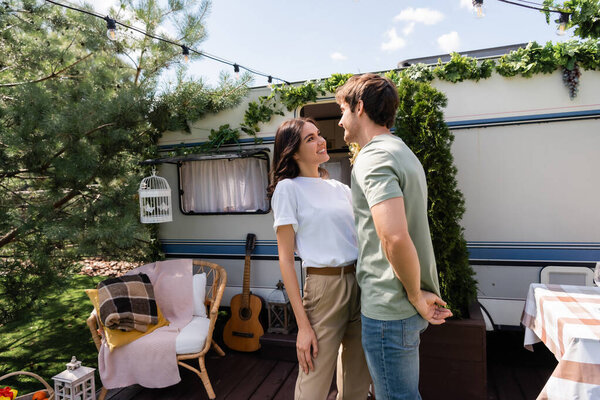 Smiling brunette couple standing on terrace near camper van 