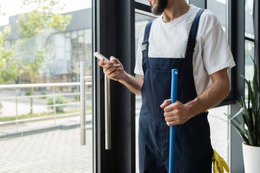 Ofiste cep telefonu kullanarak iş kıyafetlerindeki profesyonel temizleyici görüşü