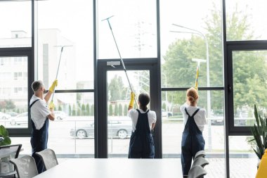 Ofiste büyük panoramik pencereleri yıkayan çok kültürlü profesyonel işçilerin arka planı