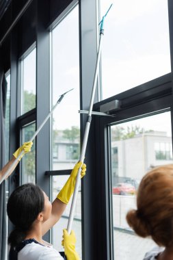 Ofisteki büyük panoramik pencereleri temizleyen lastik eldivenli profesyonel temizlikçiler.