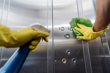Plastik eldivenli, deterjan tutan ve asansörde temizlik düğmeleri tutan temizleyicinin kısmi görüntüsü