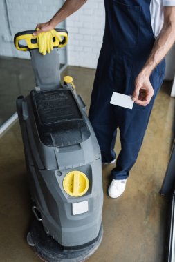 partial view of cleaner standing near floor scrubber machine and holding blank business card clipart
