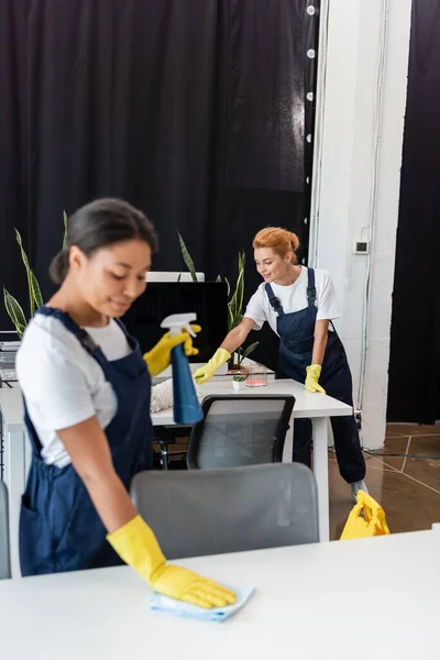 Mulheres Multiculturais Sorridentes Uniforme Luvas Borracha Limpeza Mesas Escritório — Fotografia de Stock