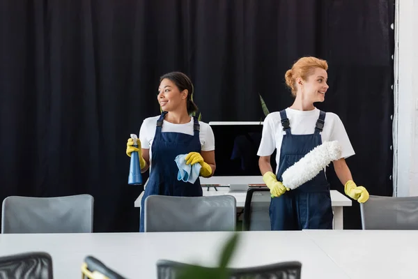 Interracial Women Overalls Holding Cleaning Supplies Smiling Office — Stock Photo, Image