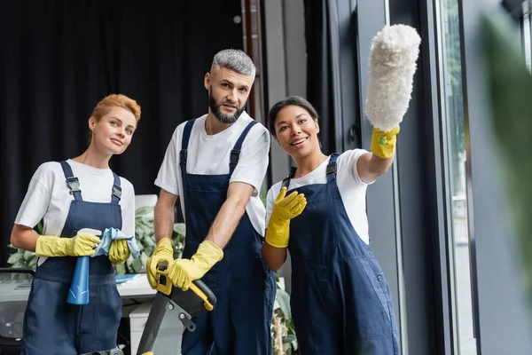 Cheerful Racial Woman Pointing Dust Brush Colleagues Cleaning Supplies — Stock Photo, Image