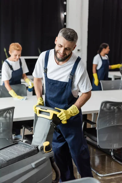 Χαμογελαστός Γενειοφόρος Άντρας Μηχανή Καθαρισμού Δαπέδων Που Εργάζεται Κοντά Διαφυλετικές — Φωτογραφία Αρχείου