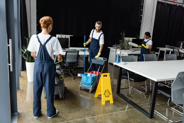女式工作服 配有地板洗涤机 靠近男人 装有清洁用品推车 — 图库照片
