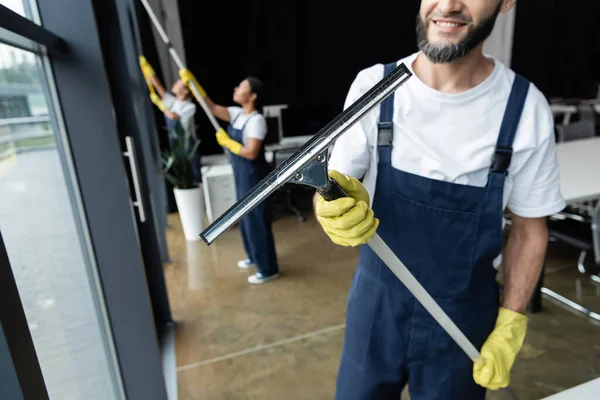 Uśmiechnięty Mężczyzna Trzyma Okno Squeegee Blisko Rozmyte Międzyrasowe Kobiety — Zdjęcie stockowe