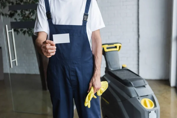 partial view of man in overalls holding empty business card near professional floor scrubber machine