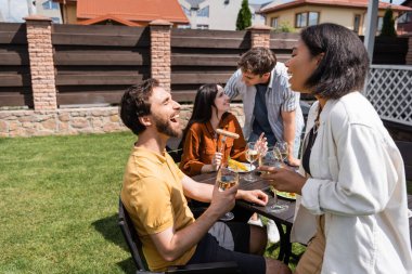 Arka bahçede yemeğin yanında gülen iki ırklı bir arkadaşın yanında şarap tutan pozitif bir adam. 