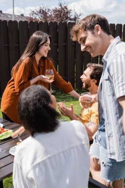 Arka bahçedeki piknik sırasında ırklar arası dostların ve şarabın yanında konuşan pozitif insanlar. 