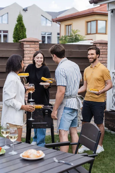 后院里 站在烤架上 用葡萄酒和盘子里的食物微笑着多种族朋友 — 图库照片