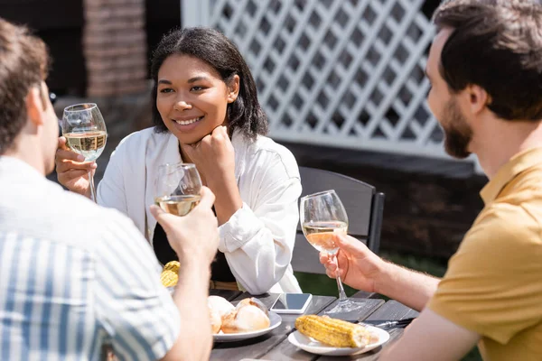 Sorridente Donna Razziale Possesso Bicchiere Vino Vicino Amici Offuscati Cibo — Foto Stock