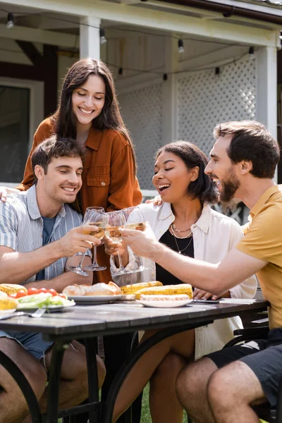 ピクニック中にグリルフードの近くでワインで乾杯する陽気な多民族の友人屋外 — ストック写真