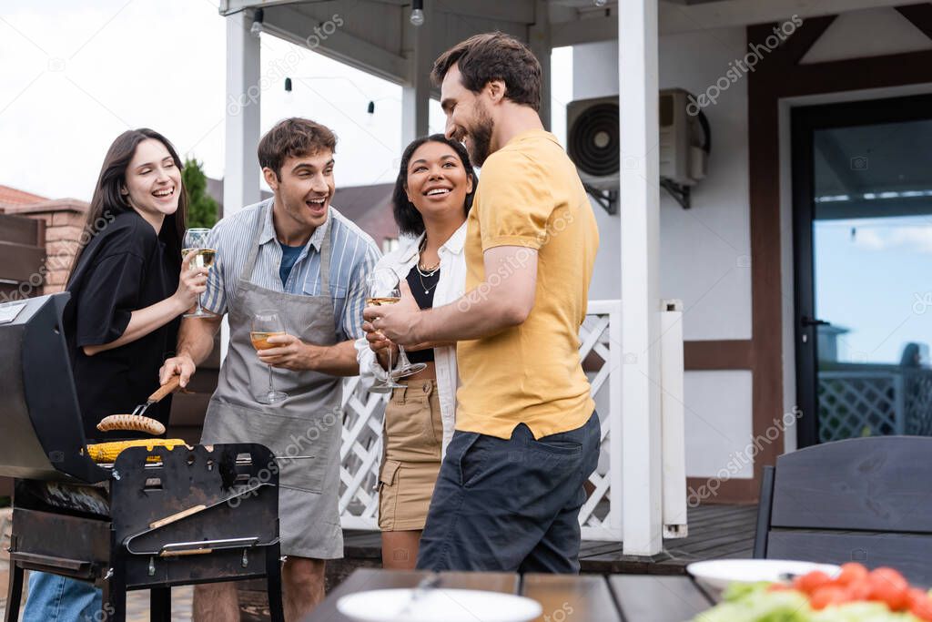Cheerful interracial friends preparing food for bbq during party on backyard 
