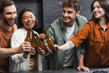 KYIV, UKRAINE - 26 Temmuz 2022: Mutlu ırklar arası arkadaşlar mutfak tezgahının yanında bira şişelerini tıkırdatıyor