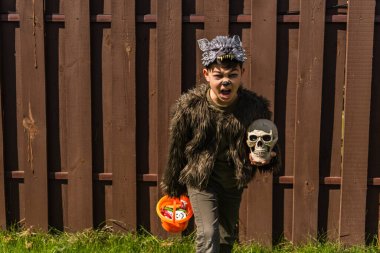 asian kid in werewolf costume holding skull and halloween bucket with sweets while showing angry grimace and growling  clipart