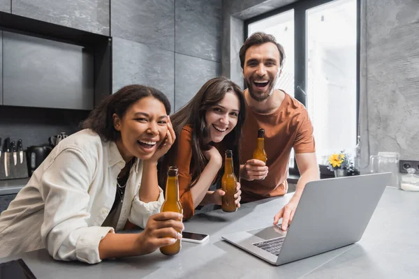 Happy Multiethnic Friends Holding Bottles Beer Gadgets Laughing Kitchen — Stock Photo, Image