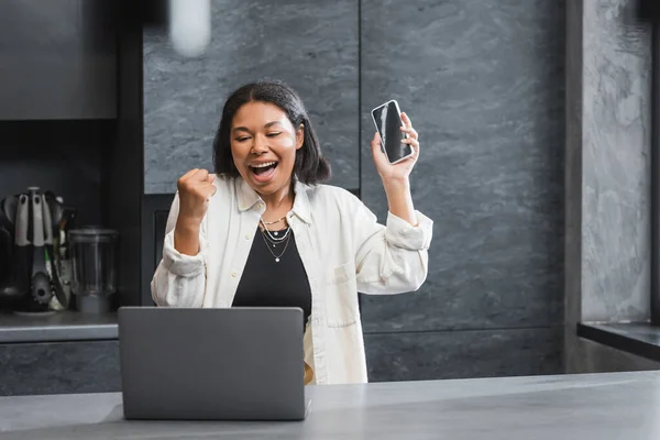 Ενθουσιασμένοι Φυλετική Γυναίκα Κρατώντας Smartphone Και Κοιτάζοντας Φορητό Υπολογιστή Στην — Φωτογραφία Αρχείου