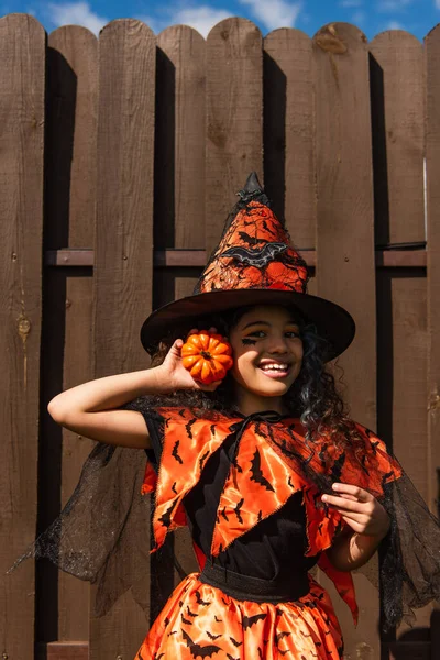 Cheerful Curly Girl Halloween Costume Witch Hat Holding Small Pumpkin — Stock Photo, Image