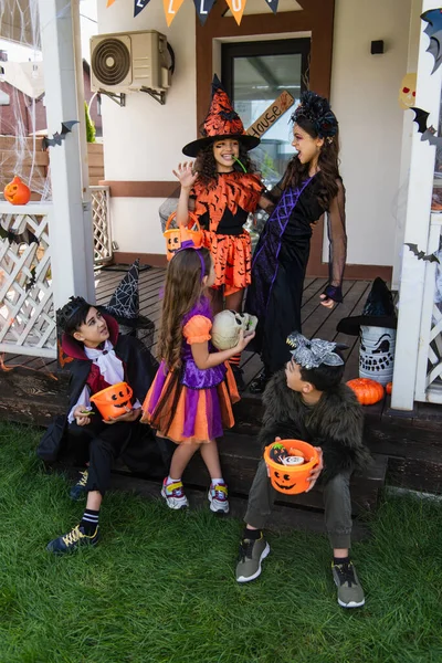 Glad Flicka Visar Skrämmande Gest Nära Multietniska Vänner Halloween Kostymer — Stockfoto