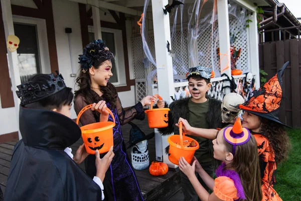 Positive Multiethnic Kids Holding Buckets Candies While Celebrating Halloween Backyard — Stock Photo, Image