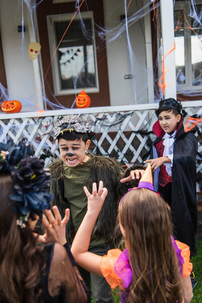 Asian boy in halloween costume grimacing near blurred friends in backyard 