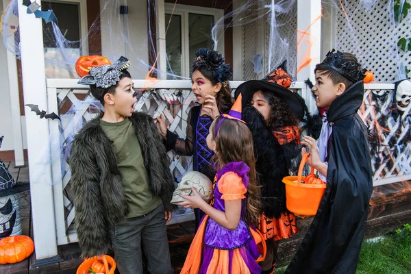Børn Kostumer Grimasser Nær Asiatisk Ven Med Spand Nær Halloween - Stock-foto